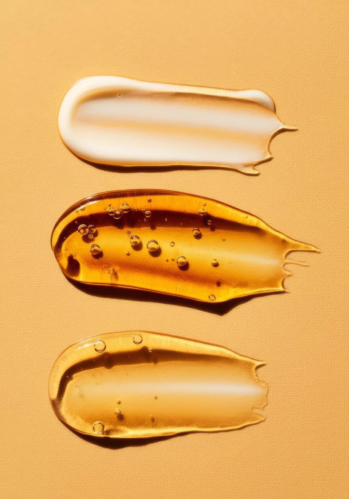 Three skincare product swatches on a golden background — a white cream, an amber serum, and a clear gel — representing different acne treatment formulas