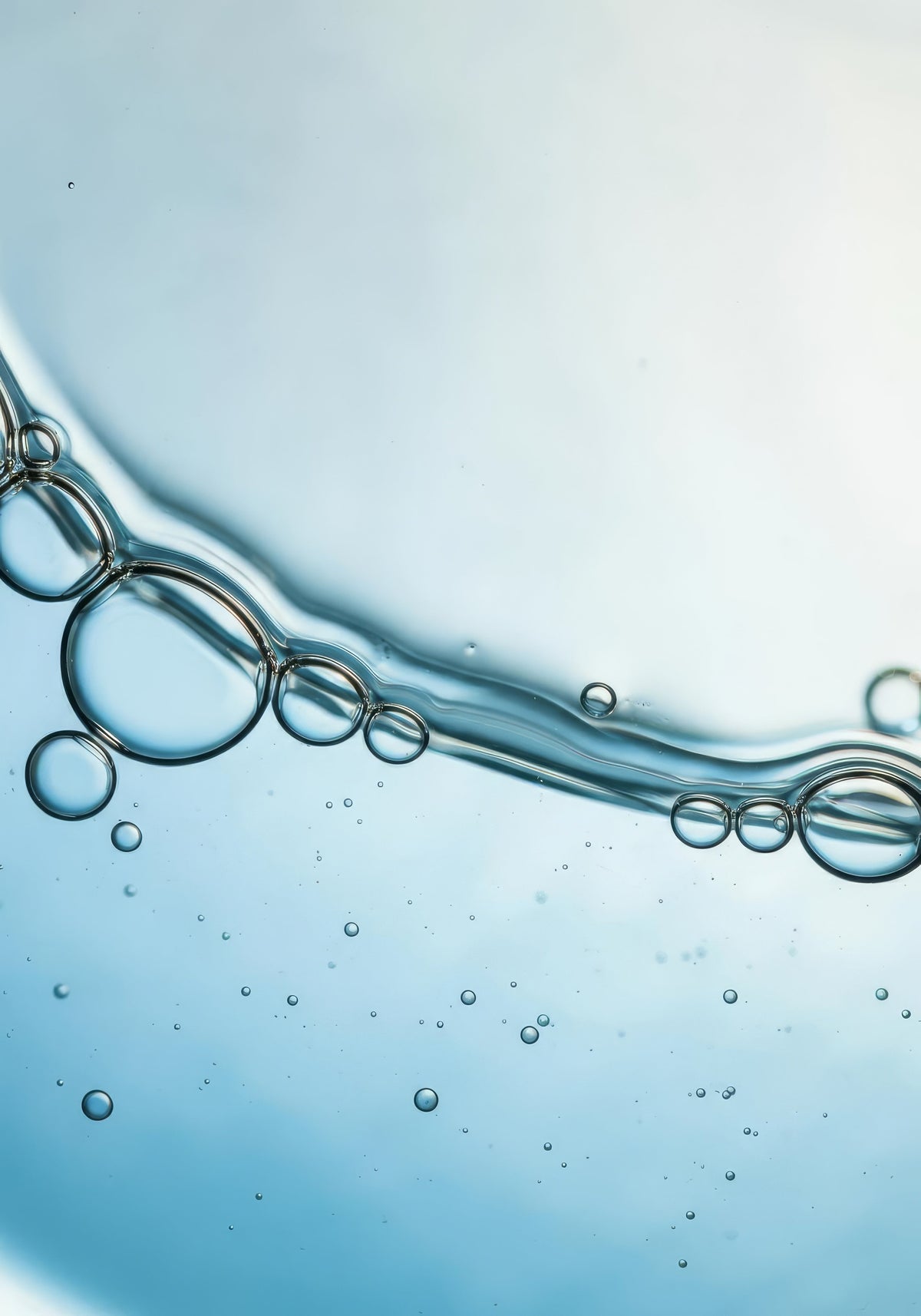 Macro close-up of bubbles and oil droplets suspended in clear liquid on a light blue background, representing clogged pores and cystic acne beneath the skin